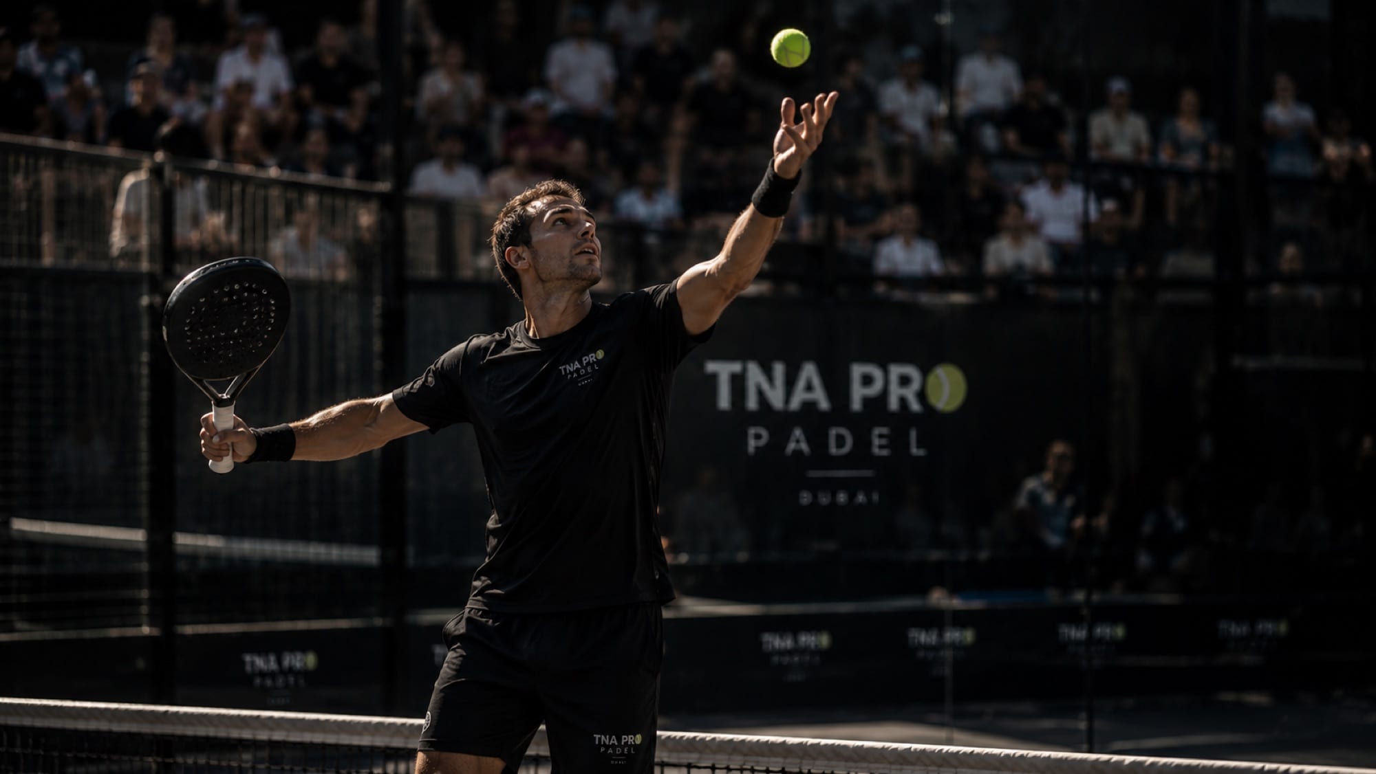 A player tossing the ball to serve during a tournament match in front of a full grandstand